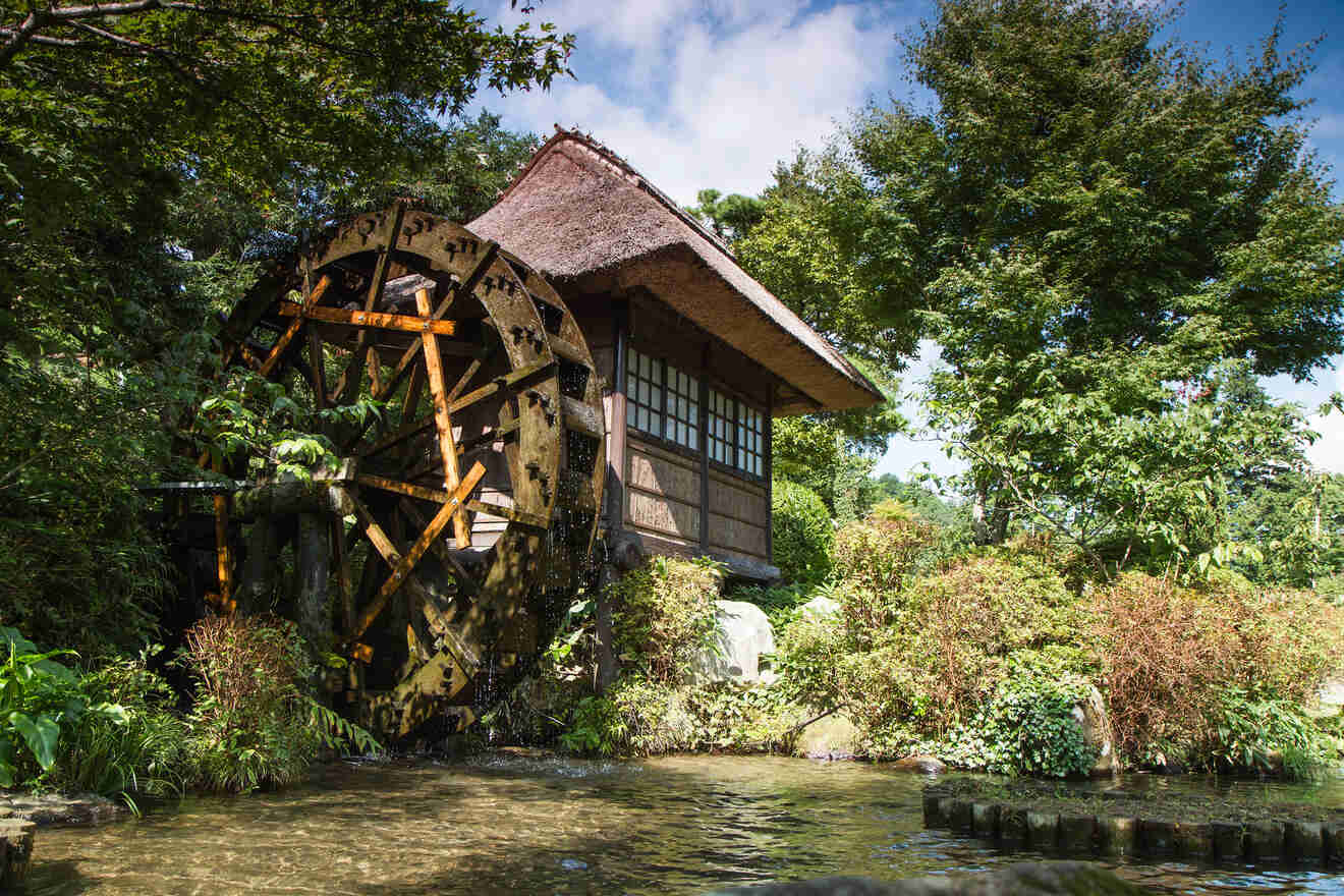Rustic watermill with a thatched-roof cottage beside a serene stream, nestled in a verdant forest setting.